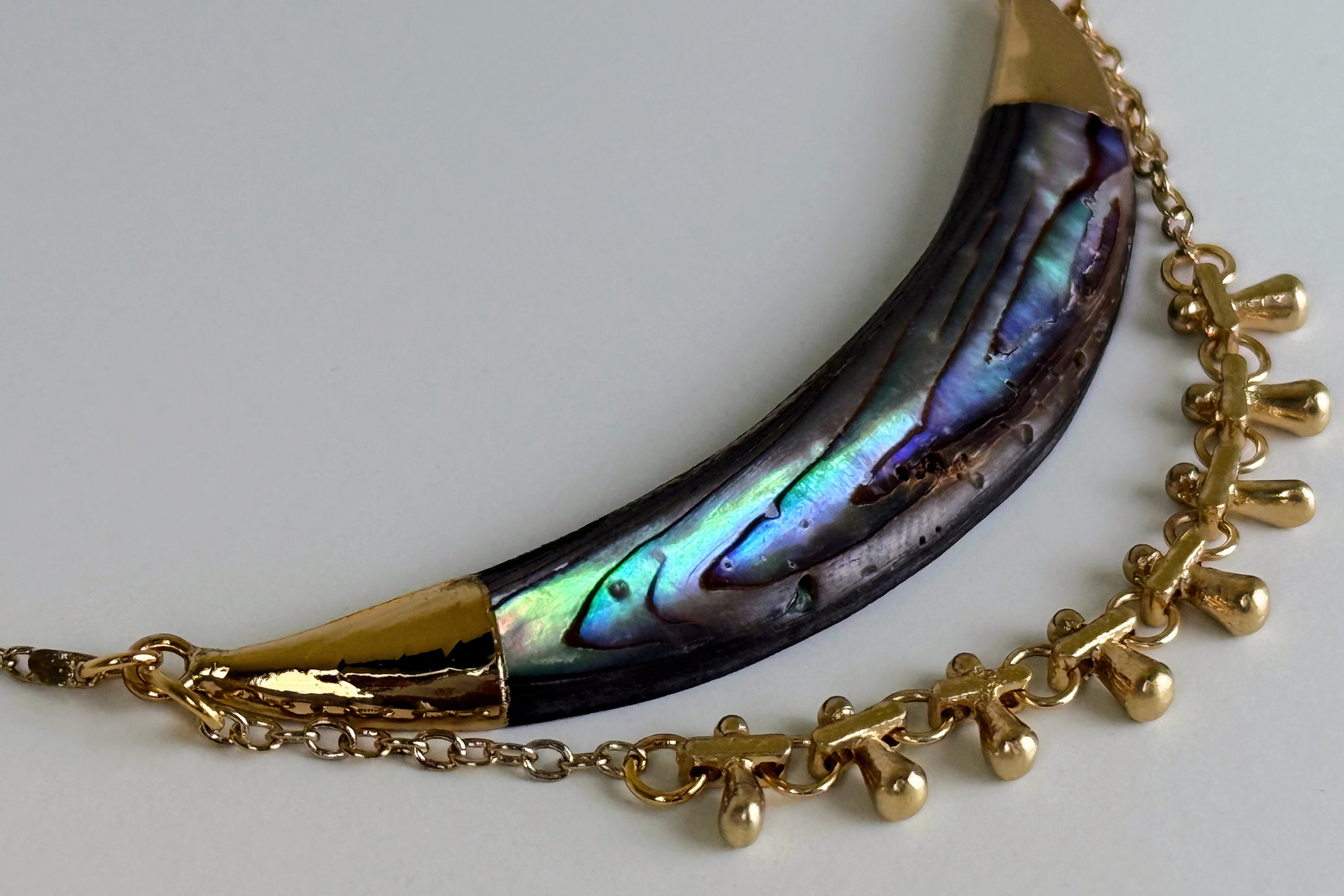 A close up image of the Darya Abalone necklace showing detail of abalone shell and gold chain with drops.