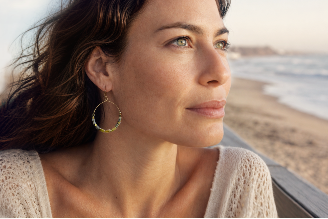 Woman with hoop earrings looking out at the ocean on a beach