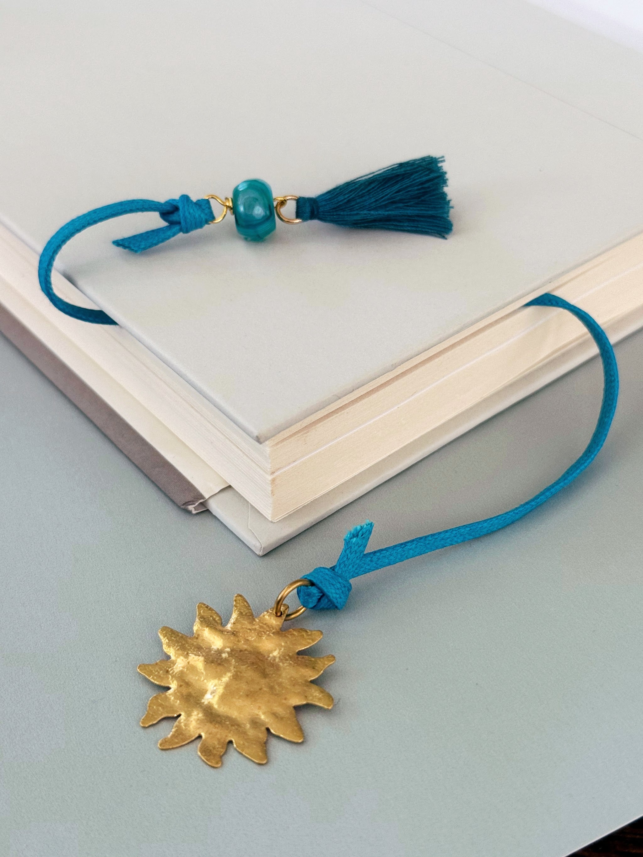 Blue tassel corded Solene bookmark with agate and a gold sun charm extending from a book.