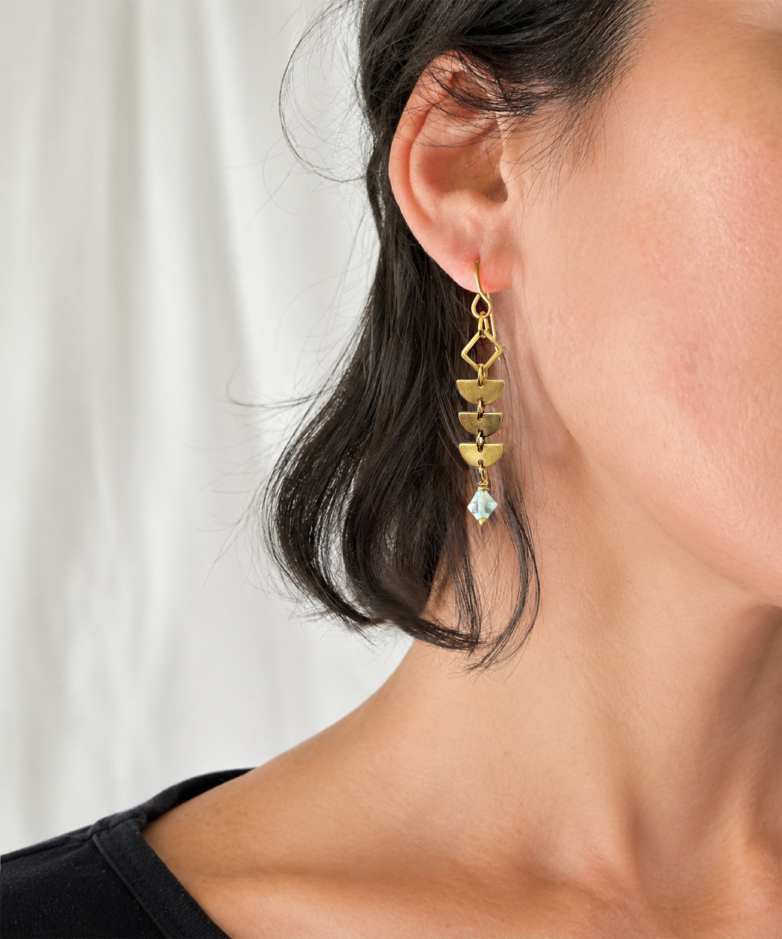 Close up of woman wearing brass Alune Fluorite Earrings shown with green fluorite. Handcrafted by Alysian.