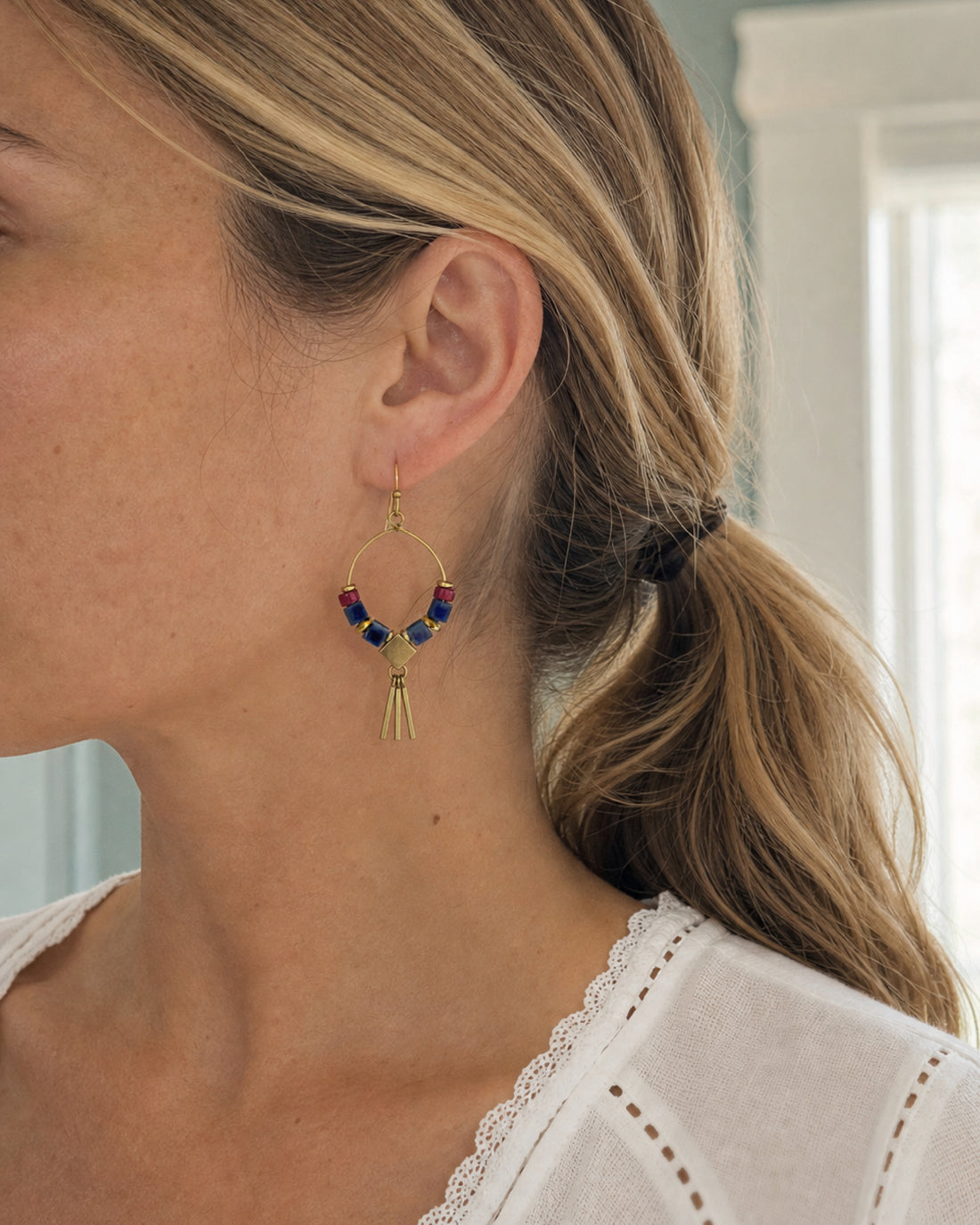 Close-up of a woman wearing a the geometric metal fringe Azra Sodalite Hoop Earring, handcrafted by Alysian.