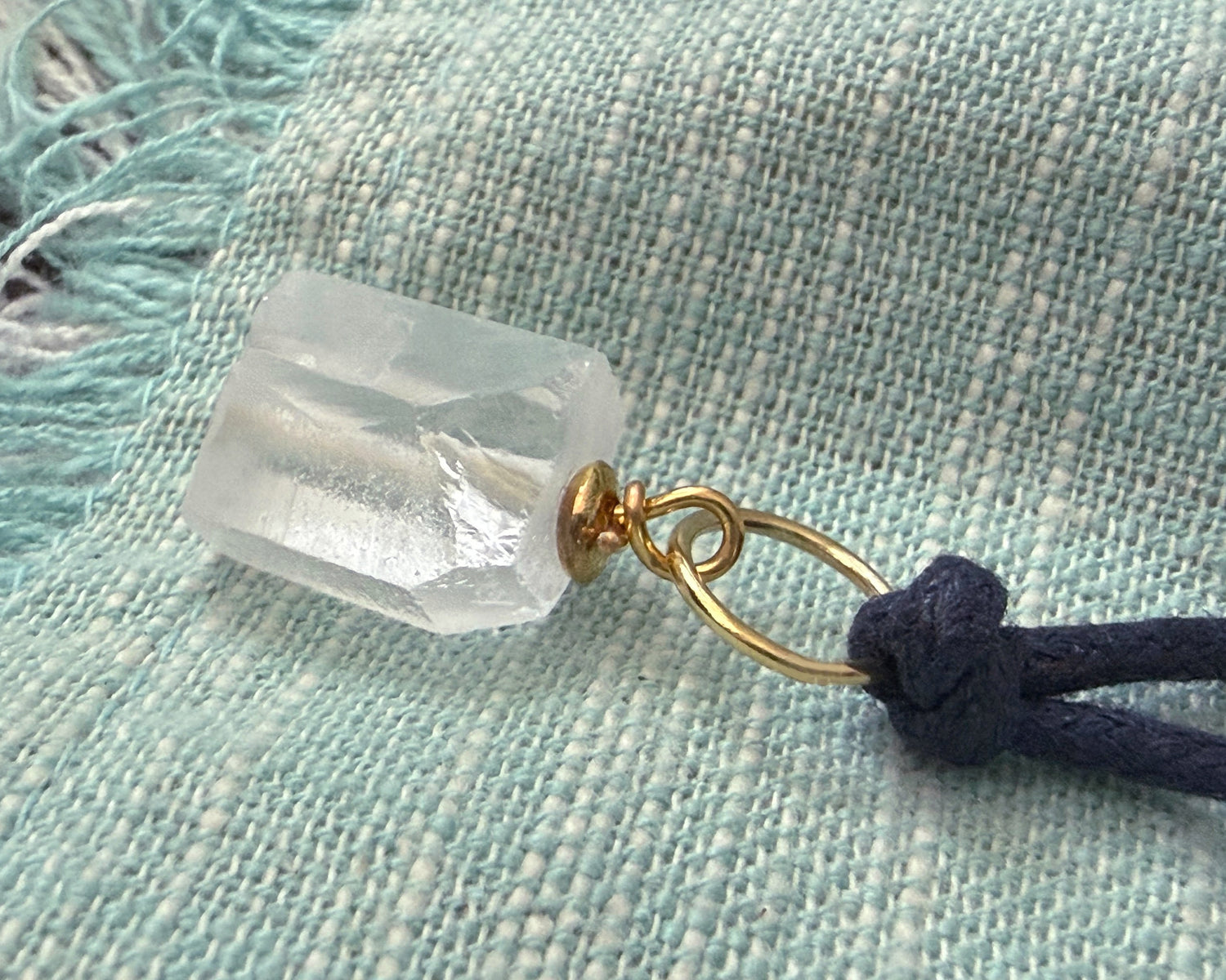 Raw crystal stone nugget on a navy blue cord against a textured fabric background.