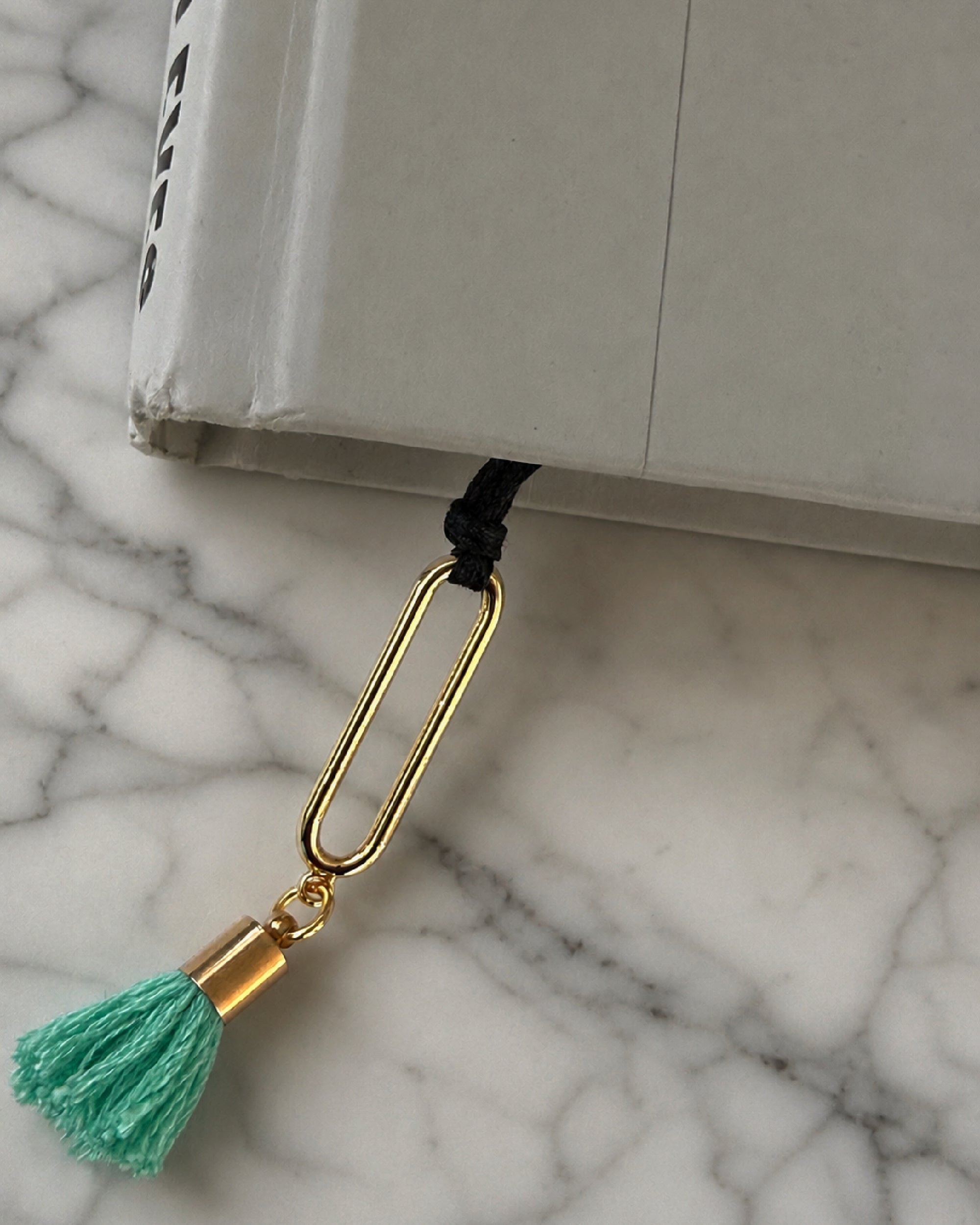 The mint green tassel of the Erris bookmark coming out of the corner of a book set on a marble surface.