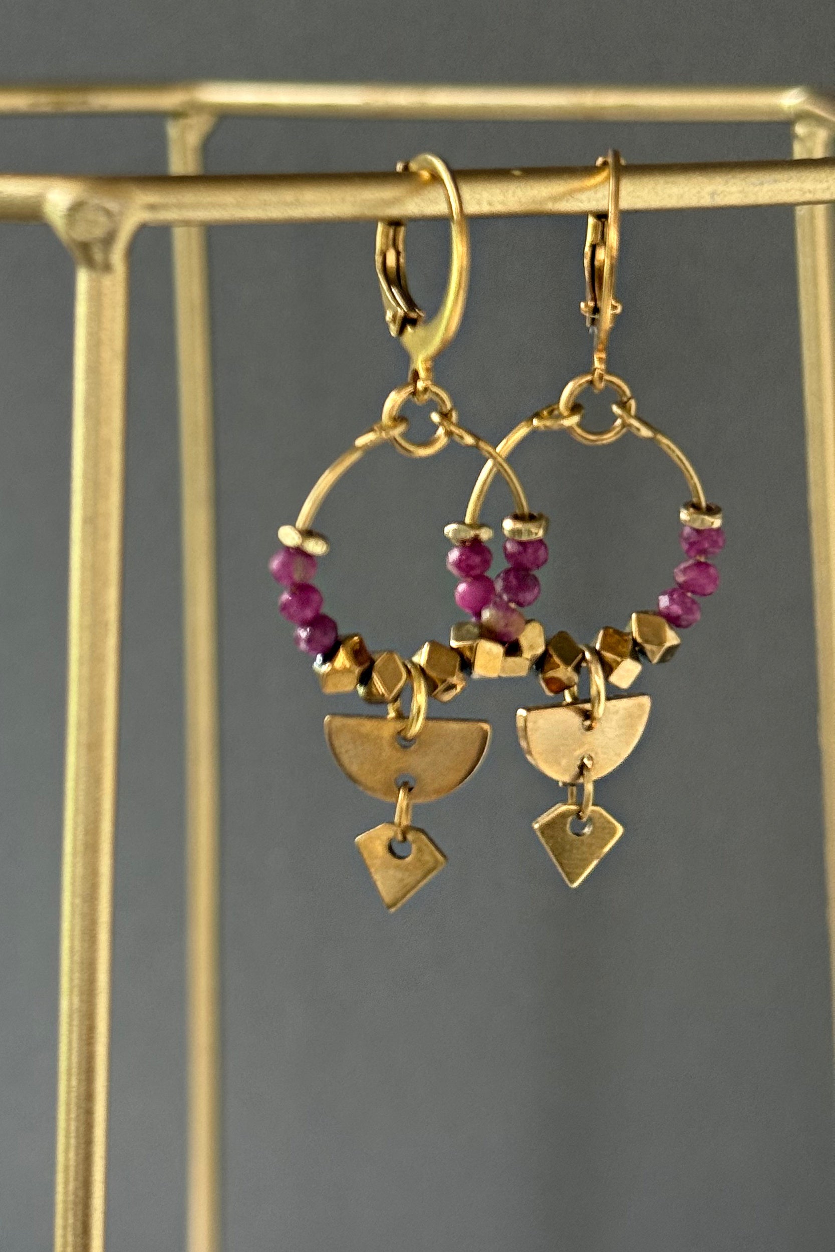 Brass hoop earrings with surgical steel leverbacks and ruby gemstones with sleek styling and boho-chic vibes shown on an earring stand — Islene ruby hoop by Alysian.