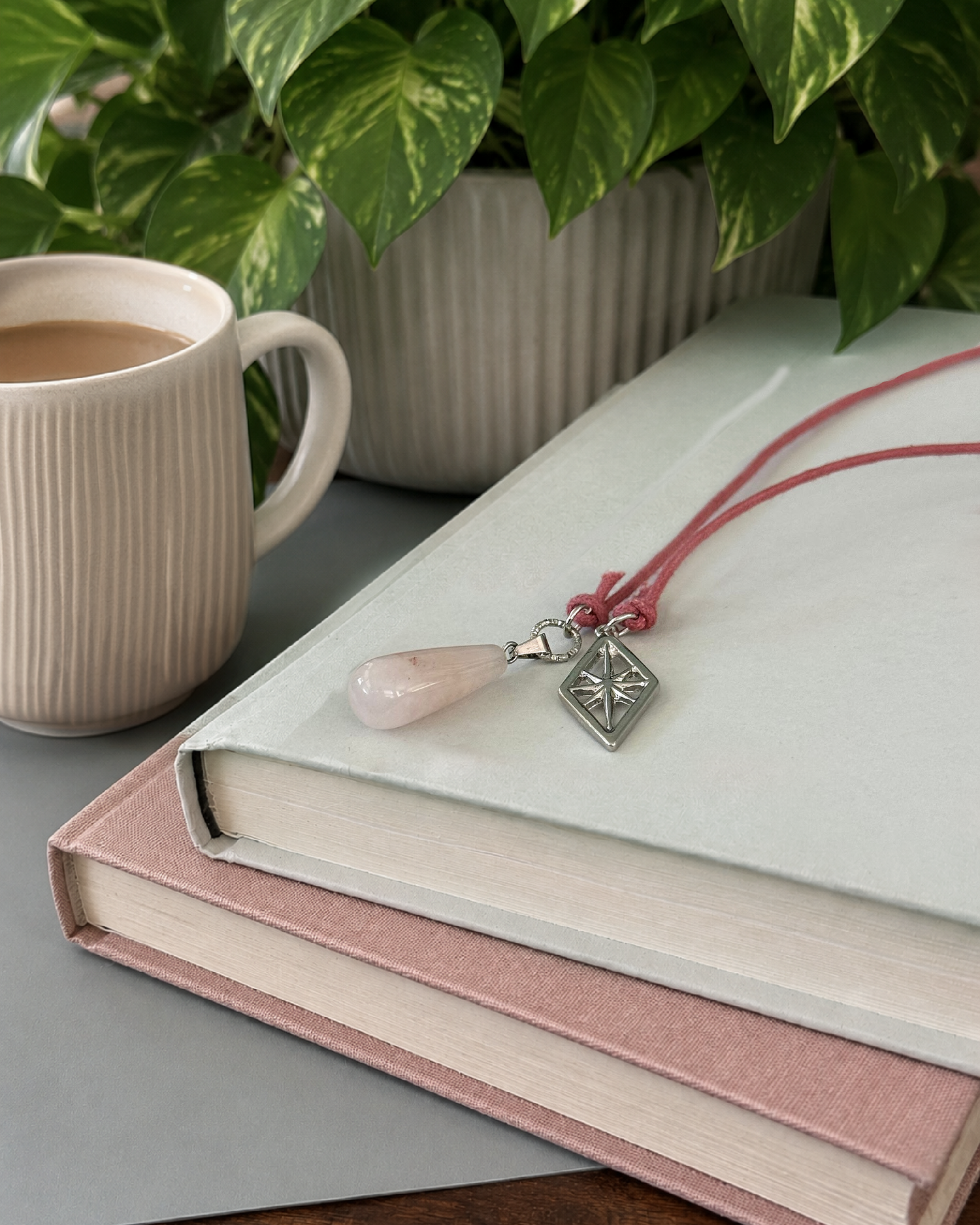 Alysian Mayve rose quartz corded bookmark laying on a book next to a cup of coffee and plant.