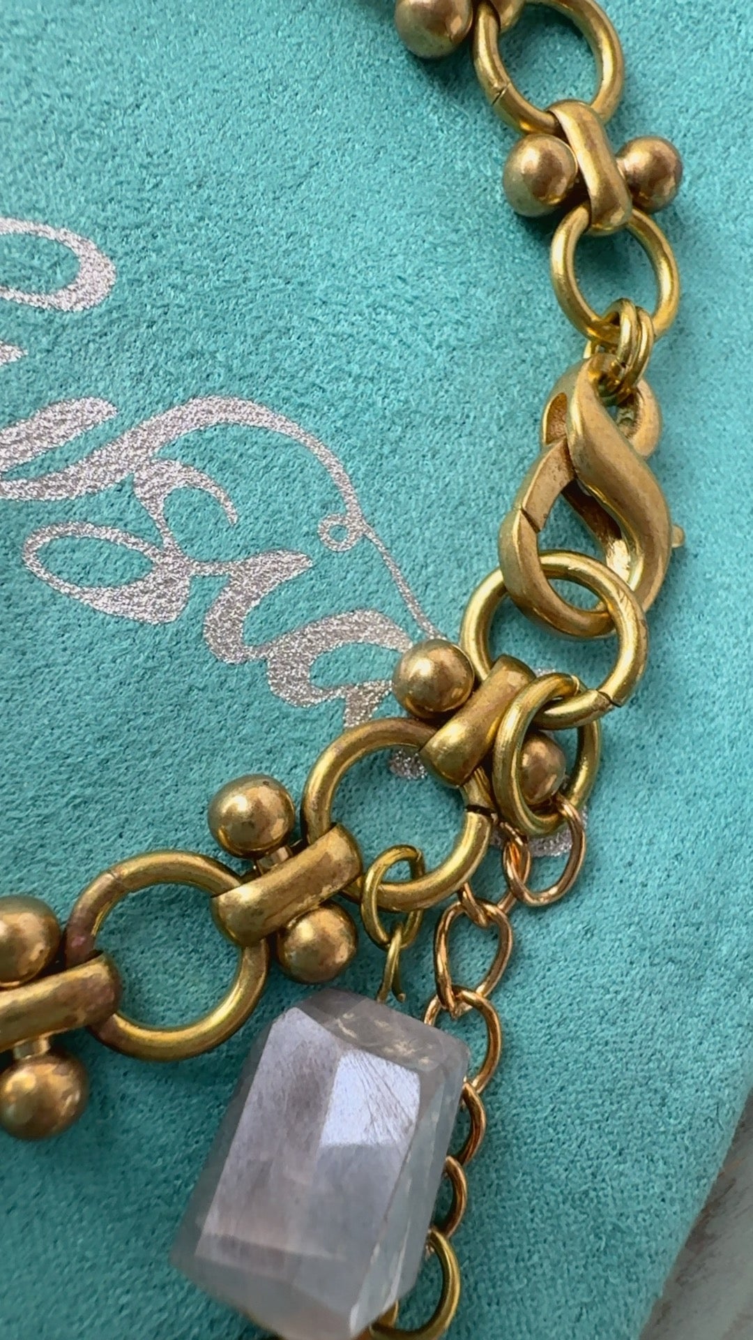 Vintage brass chain bracelet with a shimmering gray moonstone gemstone against a turquoise velvet jewelry pouch. By Alysian. #