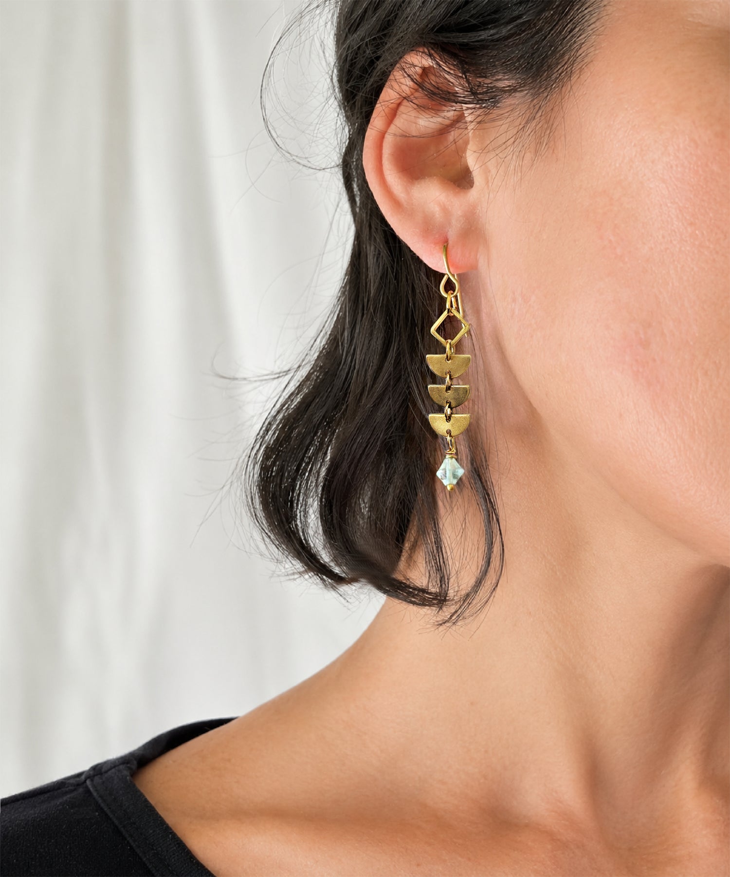 Close up of woman wearing brass Alune Fluorite Earrings shown with green fluorite. Handcrafted by Alysian.